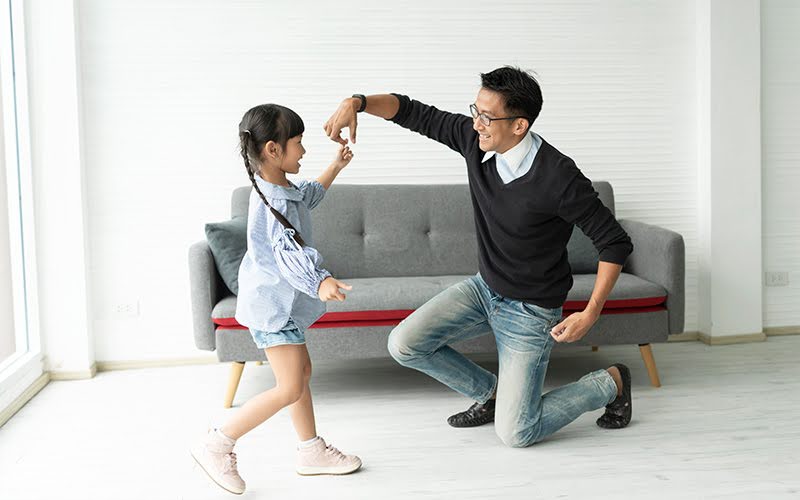 Father and daughter dancing in a living room.