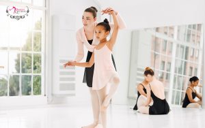 Ballet teacher guiding a young student in a studio.