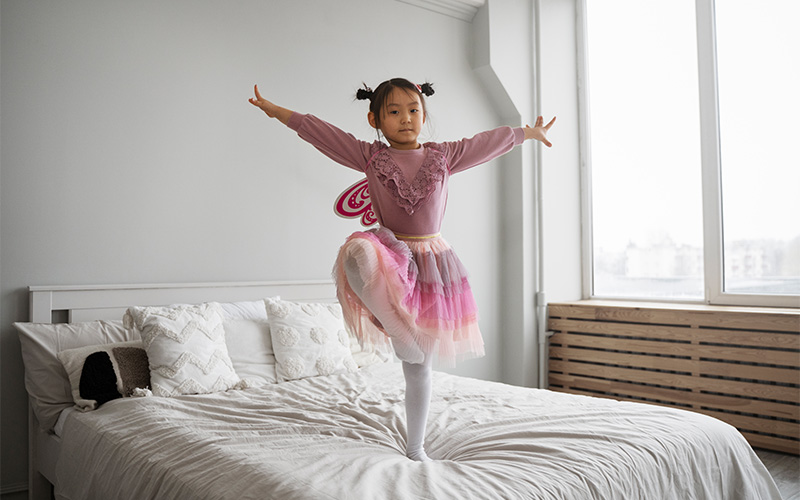 Young girl in a fairy costume dancing on a bed.